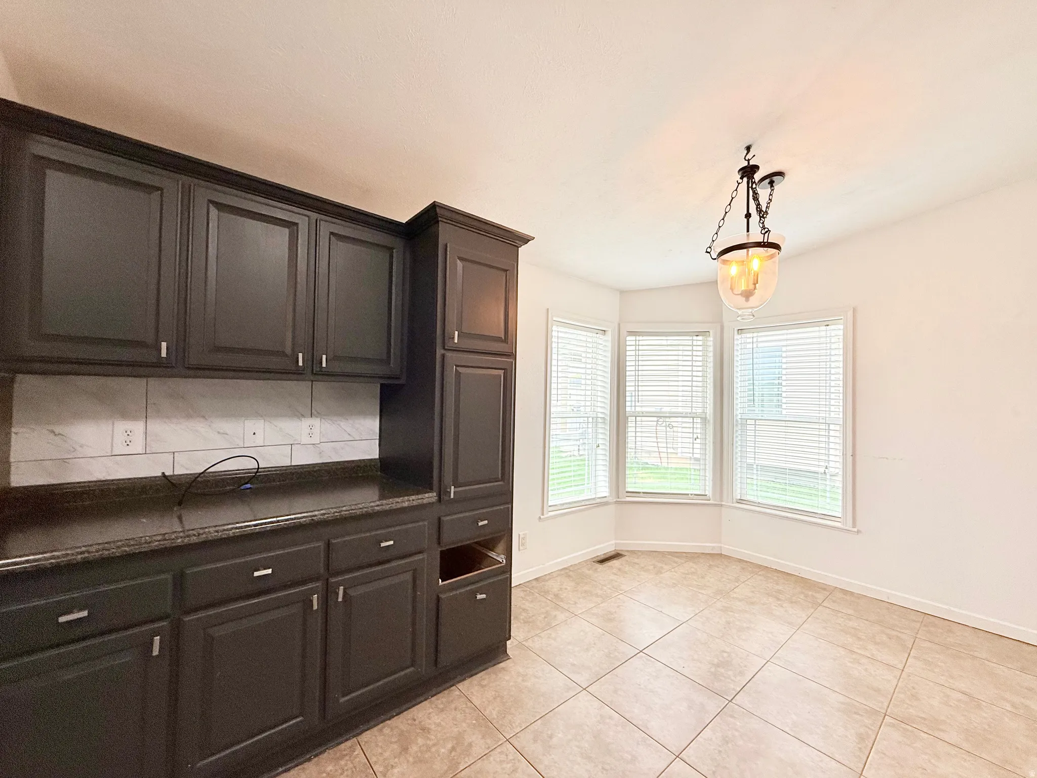 Dark cabinetry with brushed nickel hardware, a light-toned tile backsplash, and dark countertops