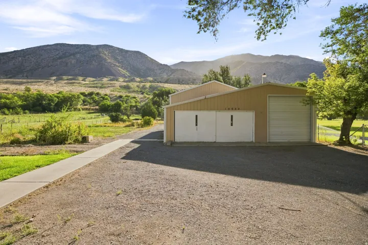 Metal structure with a light-toned exterior and a roll-up garage door, situated on a gravel surface with a concrete walkway