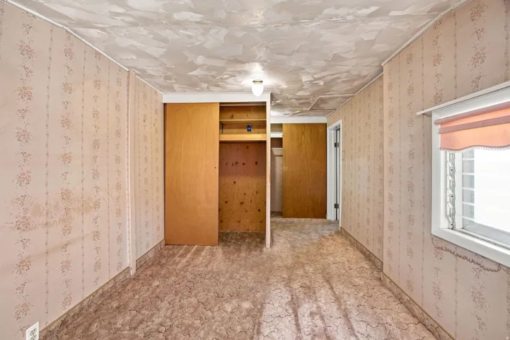Interior space with patterned wallpaper, built-in closet with sliding wood doors, and a window with a valance