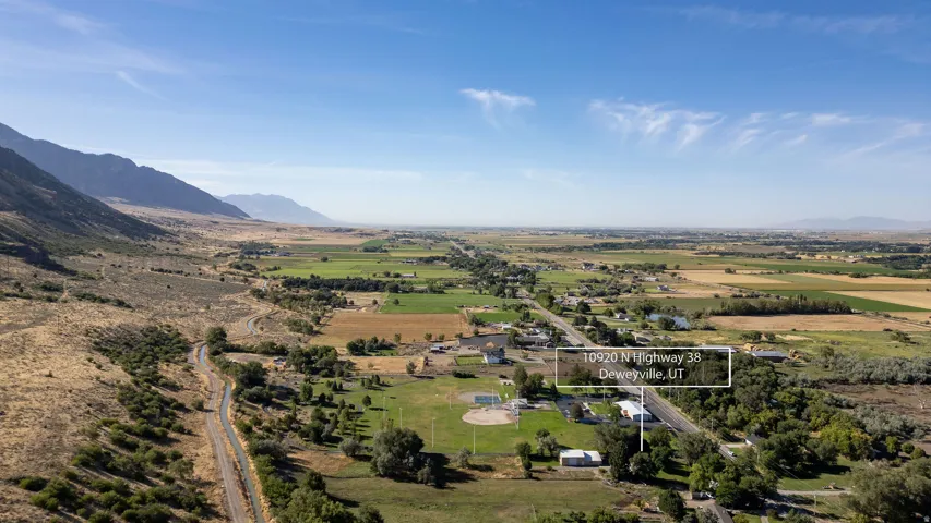 Expansive property with a mountain backdrop, featuring a paved road, scattered mature trees, and a flat, open field area