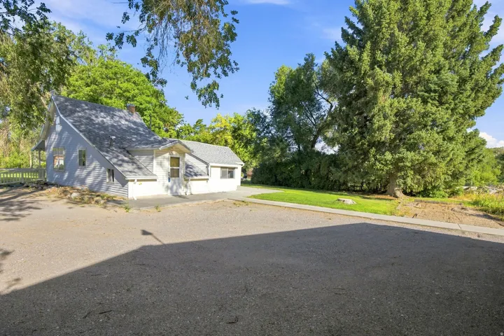 Exterior showcasing a light-colored siding, a gabled roofline, and mature surrounding trees