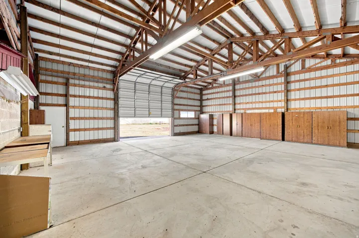 Expansive structure with exposed wood beam ceiling, concrete flooring, corrugated metal walls, and a roll-up door