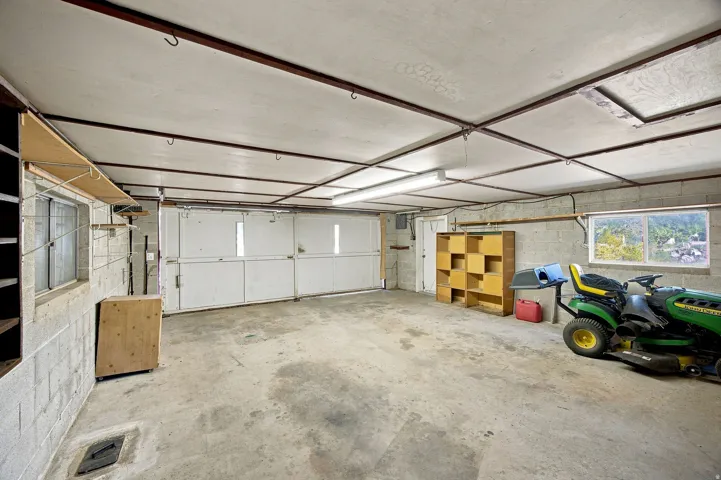 Concrete block walls with two windows, concrete flooring, overhead fluorescent lighting, and a roll-up garage door