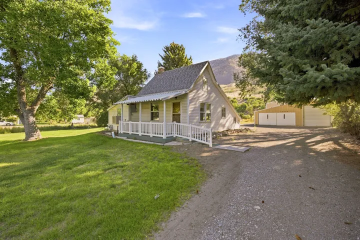 Siding exterior, covered porch with railing, sloped roofline, gravel driveway, and a detached structure with multiple garage doors