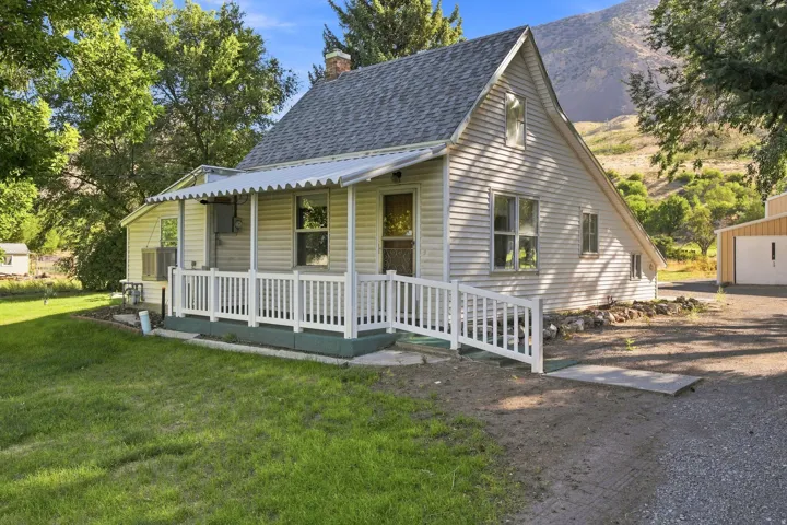 Gabled roofline, front porch with railing, exterior siding, mountain backdrop, and detached structure