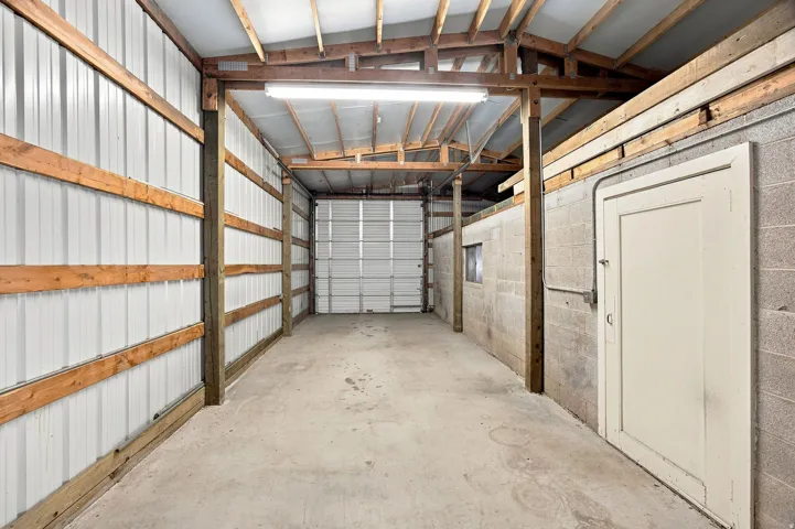 Spacious utility building featuring a concrete floor, metal siding, exposed wood beams, and a roll-up door