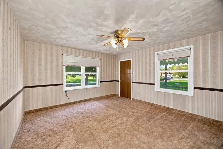 Textured ceiling, patterned wallpaper, ceiling fan with light fixture, two windows, and a wood-finish door