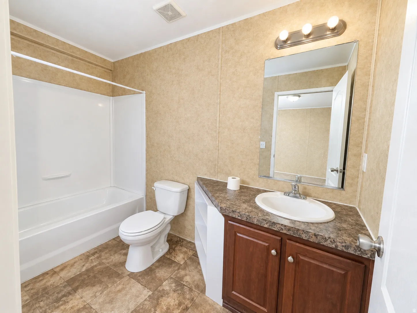 White bathtub with integrated shower, single vanity with wood-finish cabinetry, countertop with integrated sink, wall-mounted mirror, and tile-look flooring