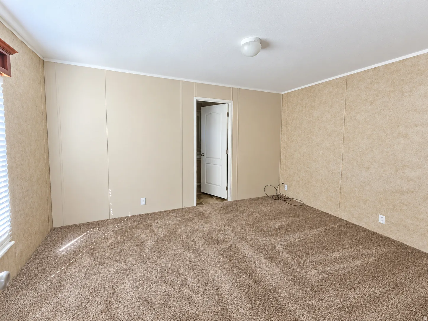 Wall-to-wall carpeting with light-toned wall panels, overhead flush mount lighting, and a white interior door