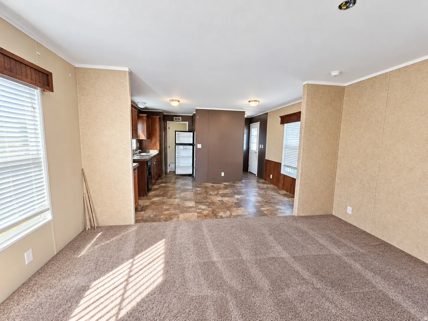 Carpeted living area with textured wall panels, white trim, and a window with blinds