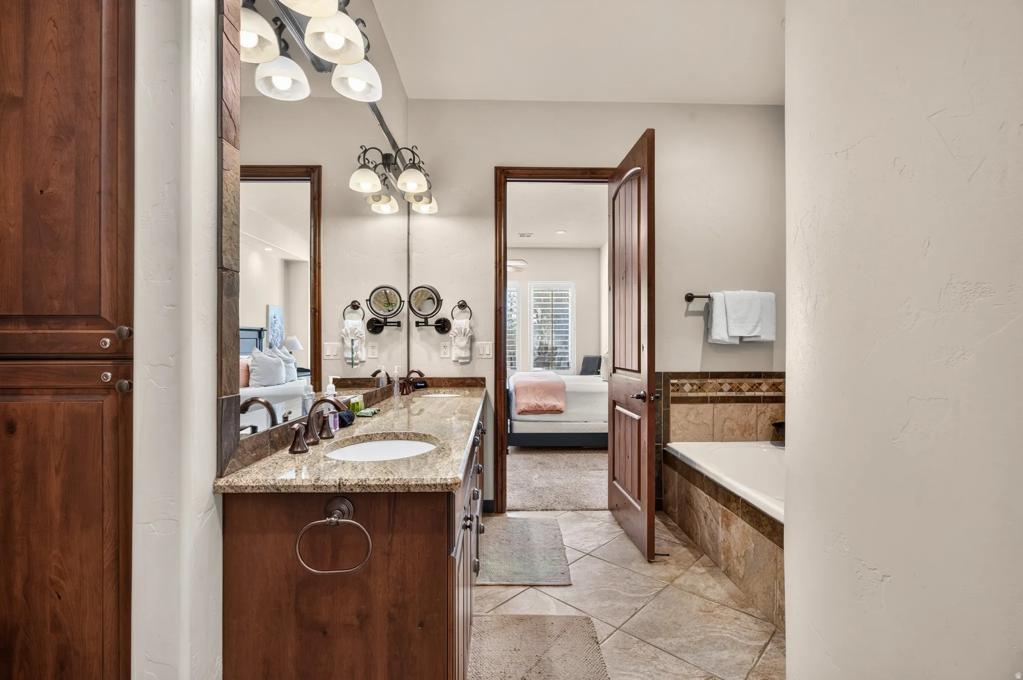 Dual vanity with granite countertop and undermount sinks, wood-finish cabinetry, and tiled flooring