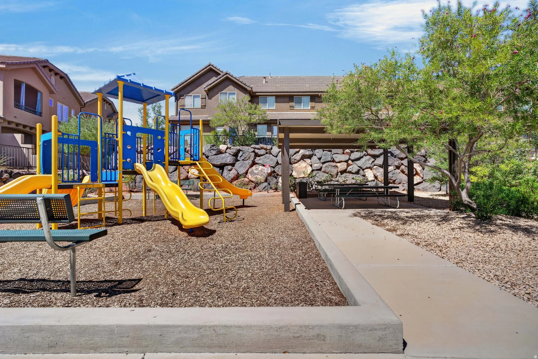 Community playground featuring multiple slides and climbing structures, shaded picnic area, and concrete pathways