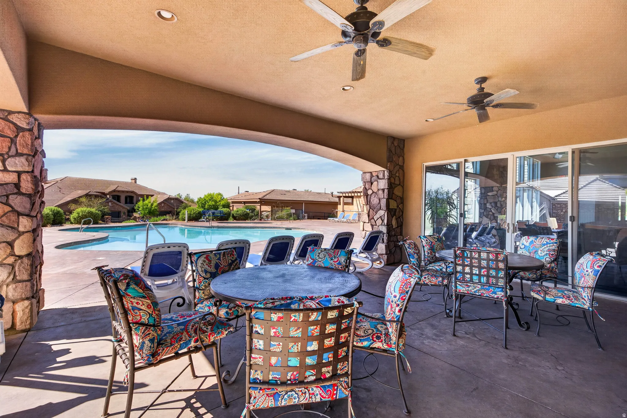 Covered patio with dual ceiling fans, stone-clad columns, and a concrete surface