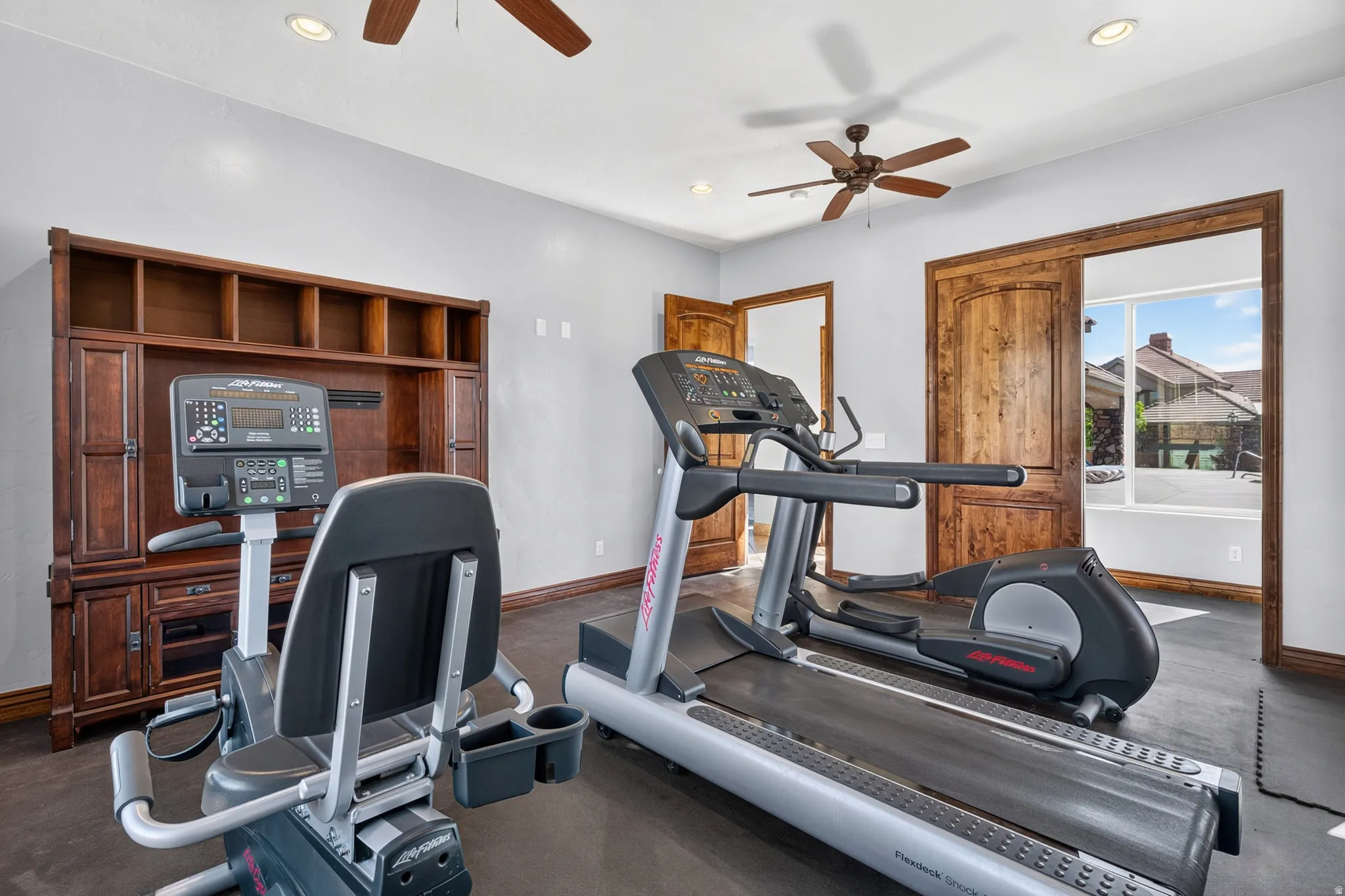Dedicated exercise room featuring a built-in wood-finish entertainment center, two ceiling fans, recessed lighting, and wood-finish doors