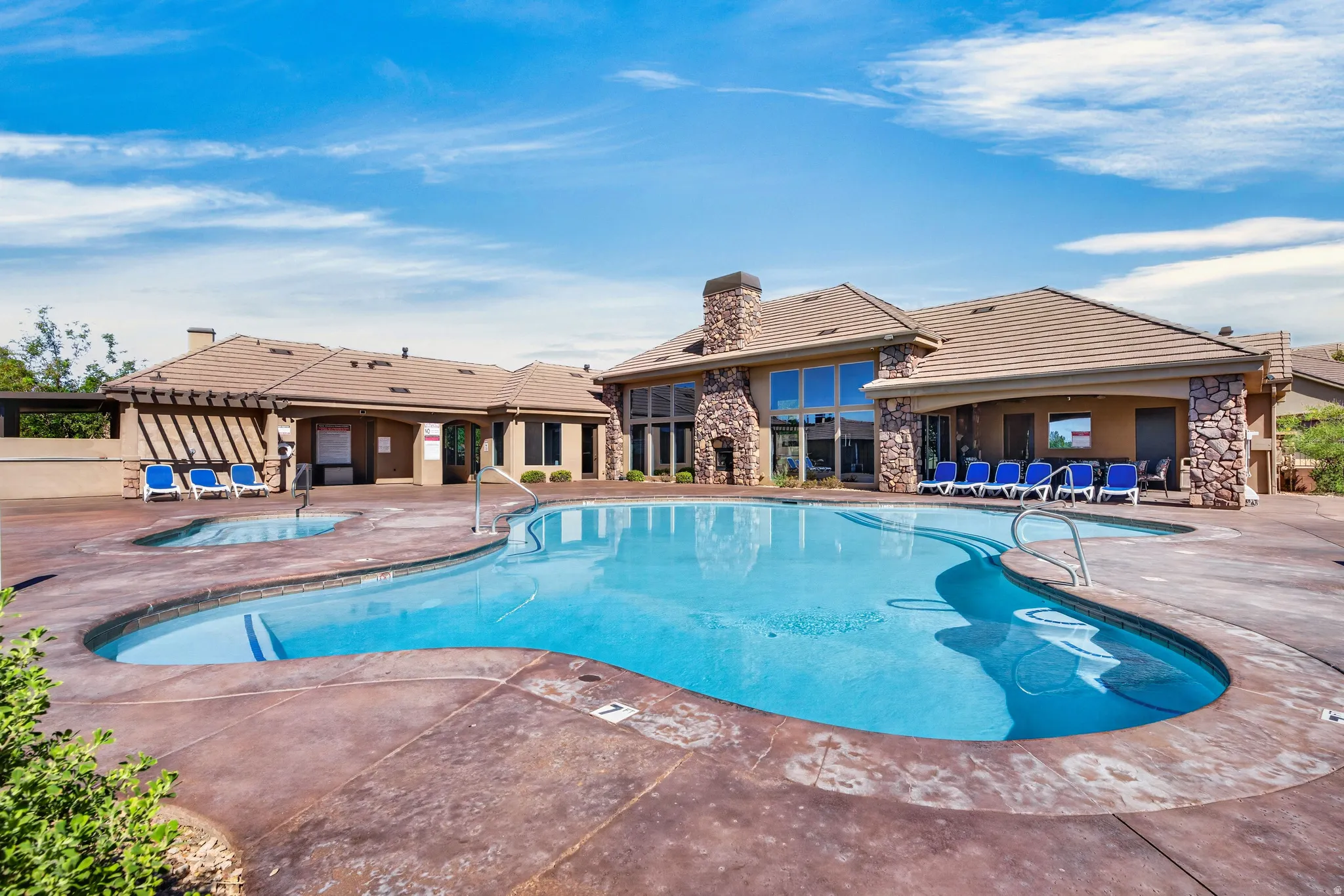 Resort-style pool with integrated spa, expansive pool deck, and a clubhouse featuring large windows and stone accents