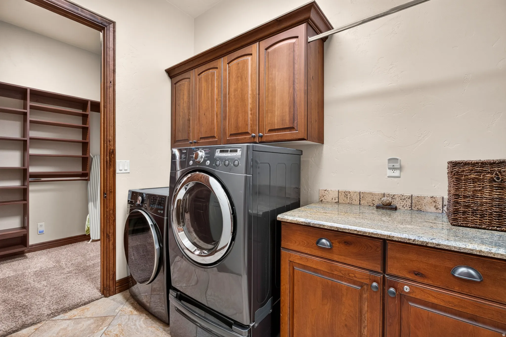 Laundry area featuring wood-finish cabinetry, granite-style countertop, and a tiled backsplash