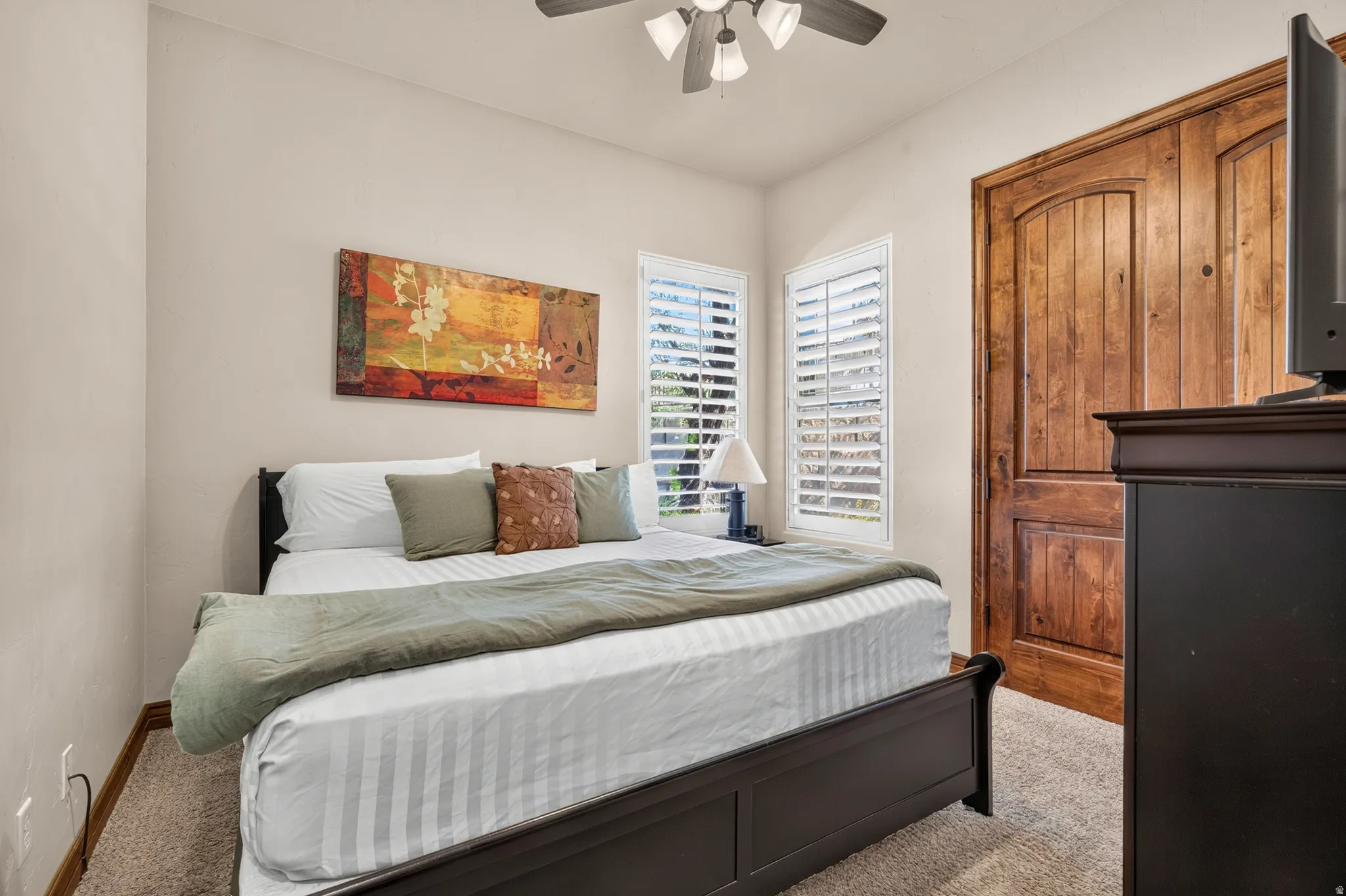 Room featuring a ceiling fan, dual windows with plantation shutters, and wood-finish doors