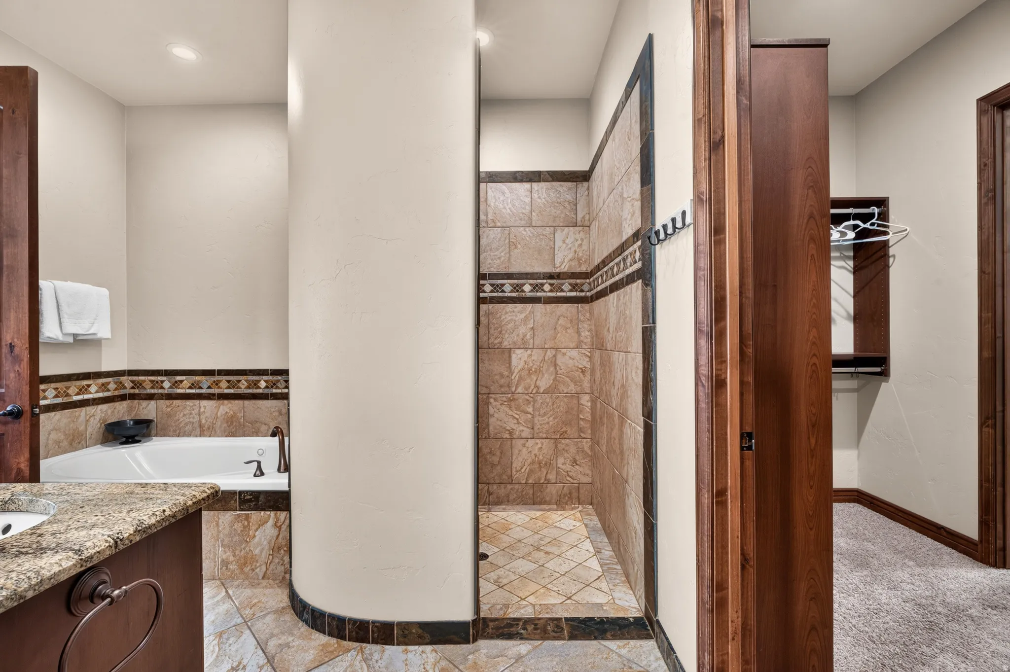 Walk-in shower with tiled walls and floor, adjacent to a built-in bathtub with tiled surround
