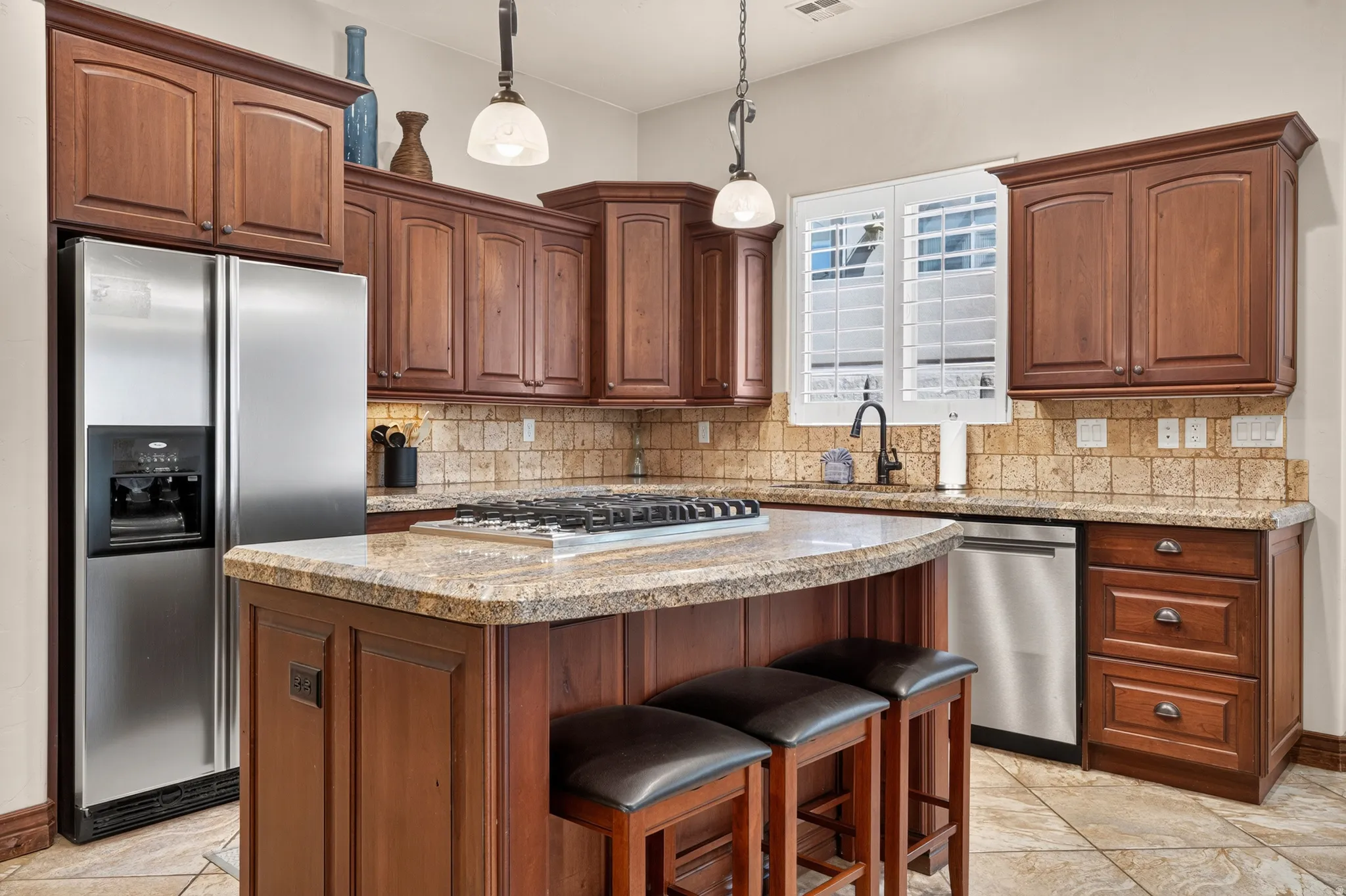 Kitchen featuring wood cabinetry, stainless steel appliances, a center island with a cooktop, granite countertops, and a tiled backsplash