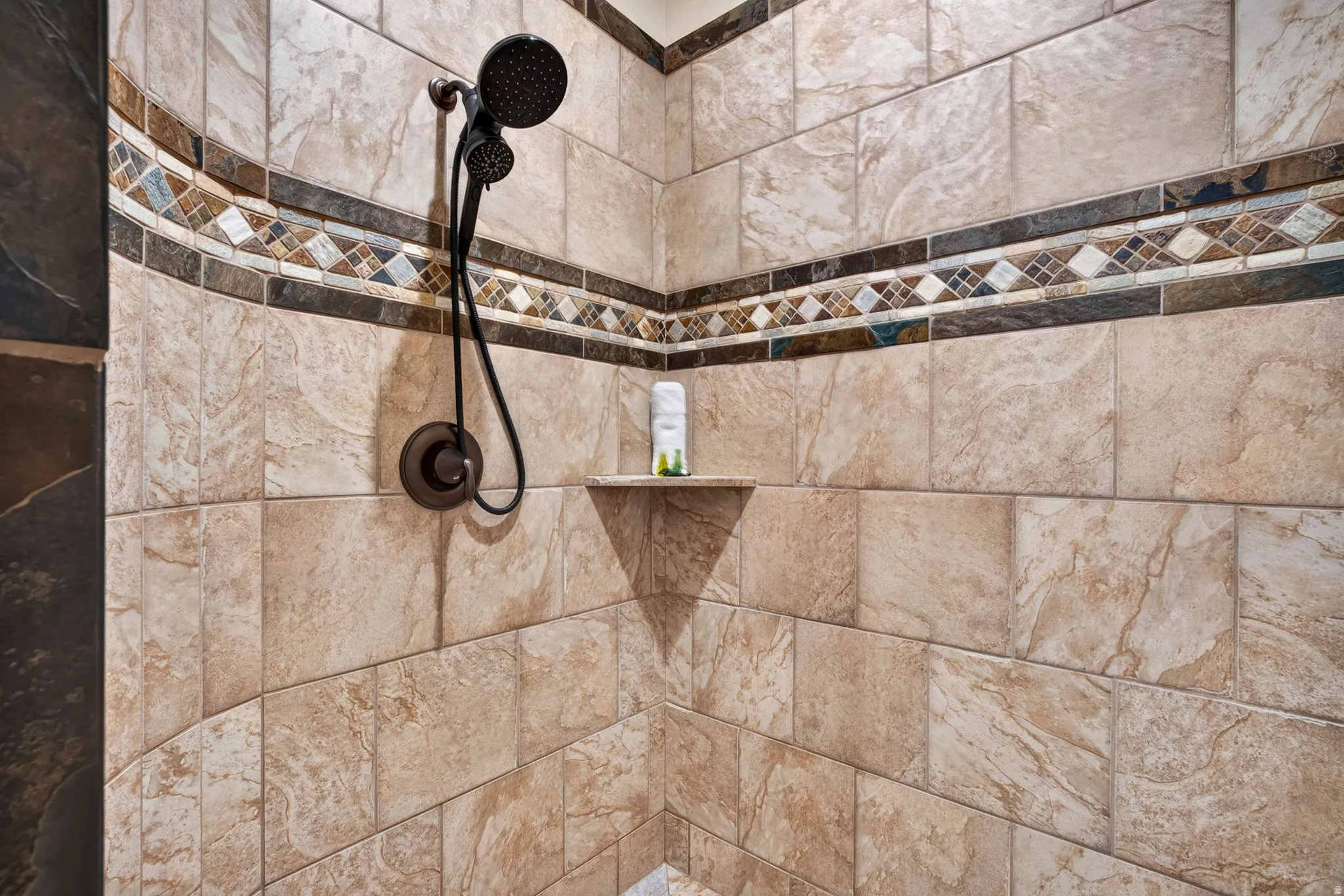 Tile shower enclosure with a mosaic accent band, integrated corner shelf, and an oil-rubbed bronze shower system