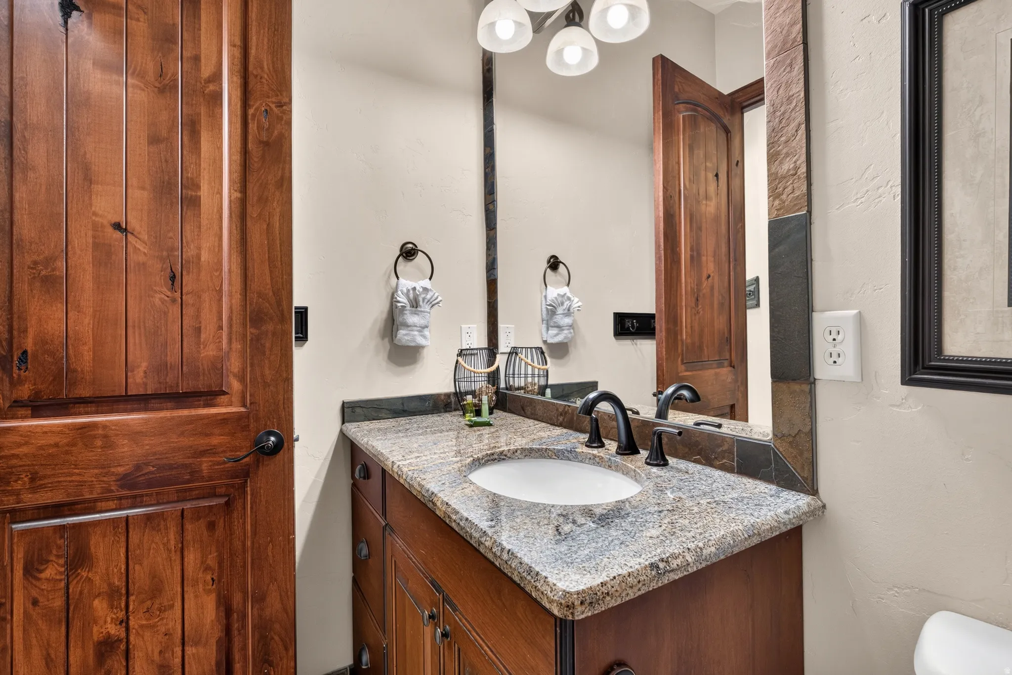 Warm wood-panel door, granite countertop vanity, integrated sink, and dark bronze fixtures