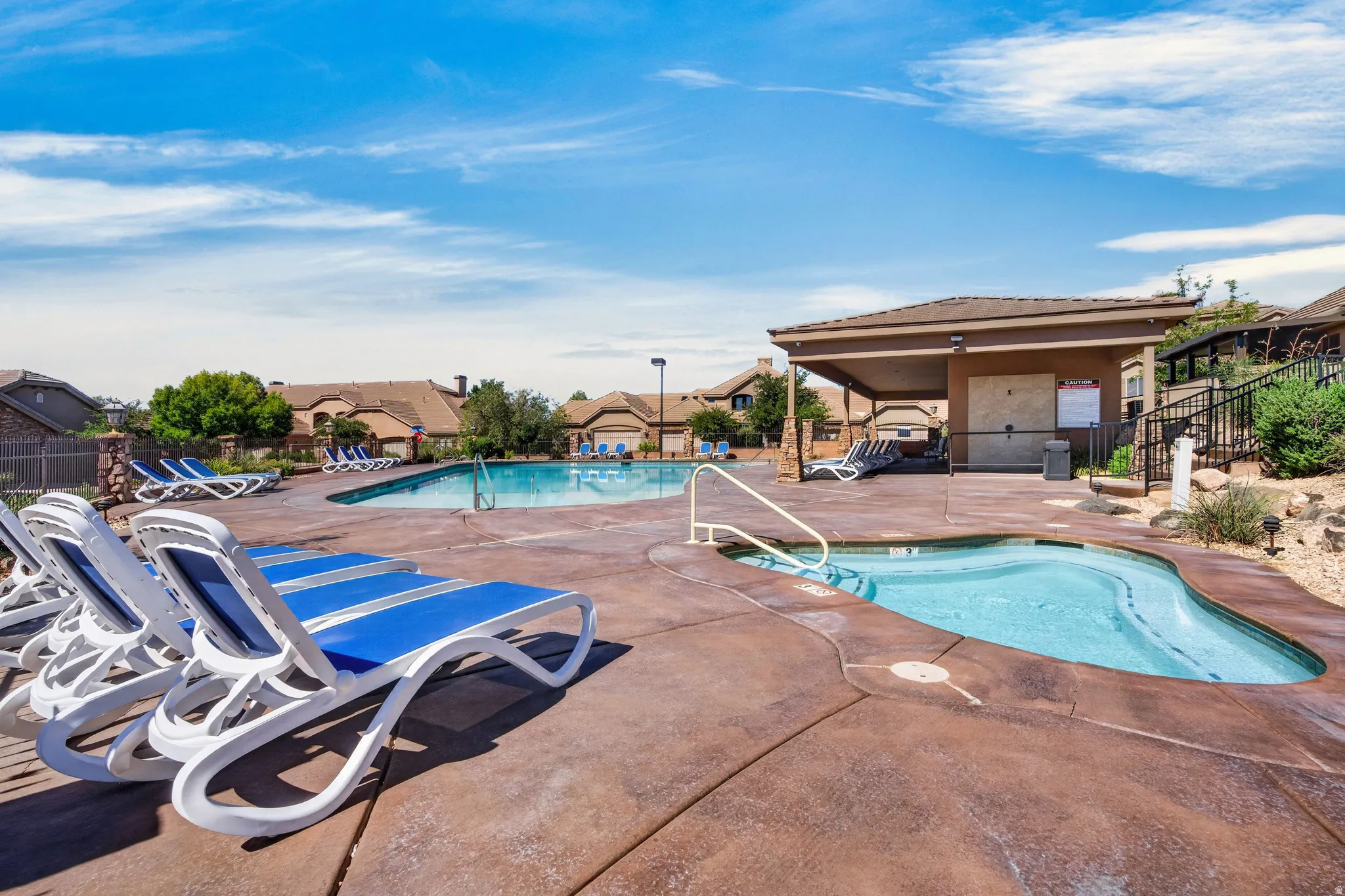 Expansive outdoor pool area featuring a large swimming pool, an integrated spa, a covered cabana structure, and a textured concrete deck