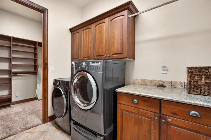 Laundry area featuring wood-finish cabinetry, granite-style countertop, and a tiled backsplash
