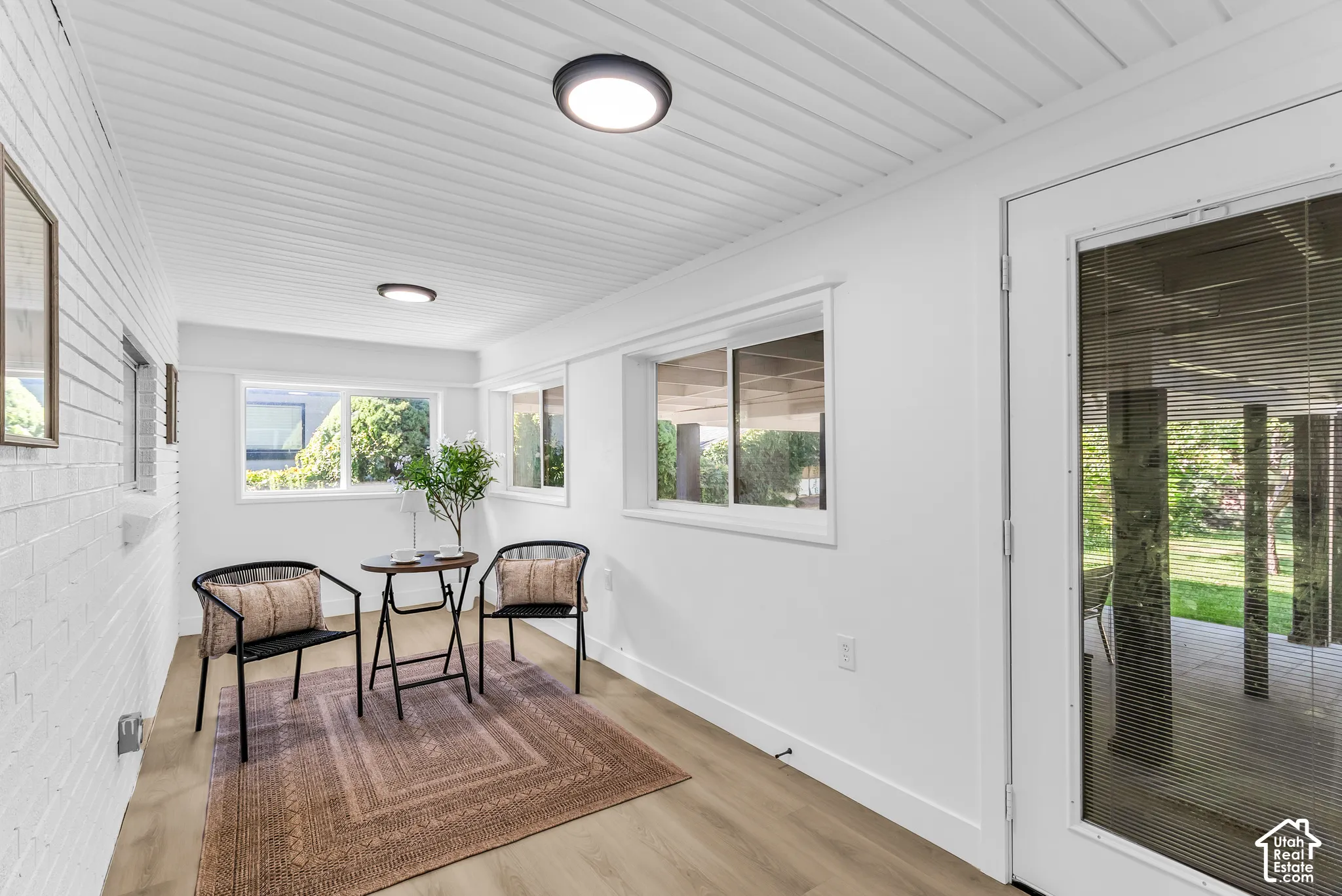 Bonus, green room, off from the kitchen. White plank ceiling with flush-mount lighting, light wood-finish flooring, white painted brick wall, and multiple windows