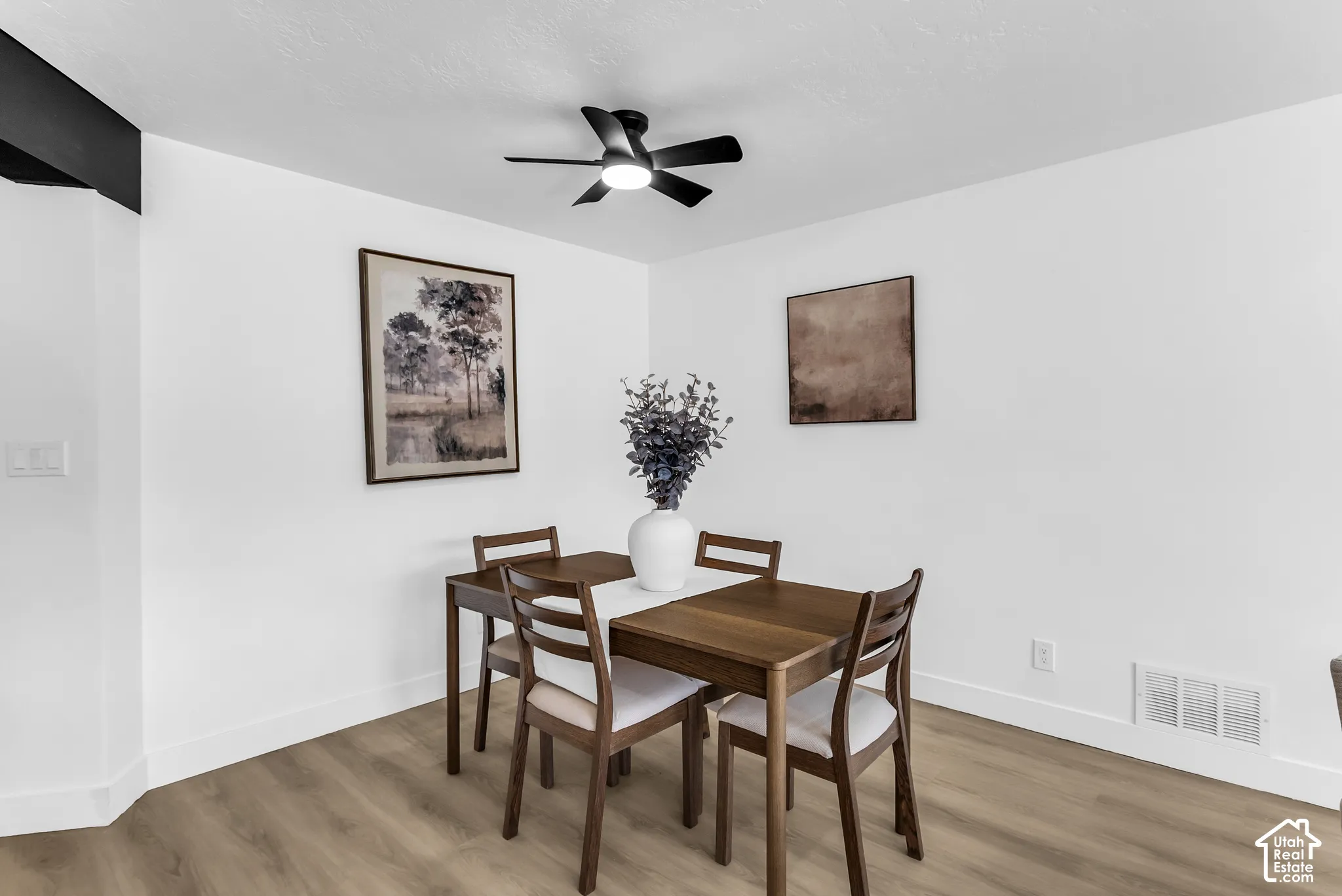 Wood-finish flooring, white walls, and a black ceiling fan