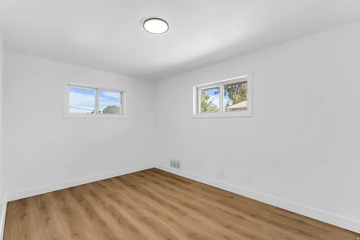 Second bedroom with two windows with white trim, wood-finish flooring, and a flush-mount ceiling light fixture
