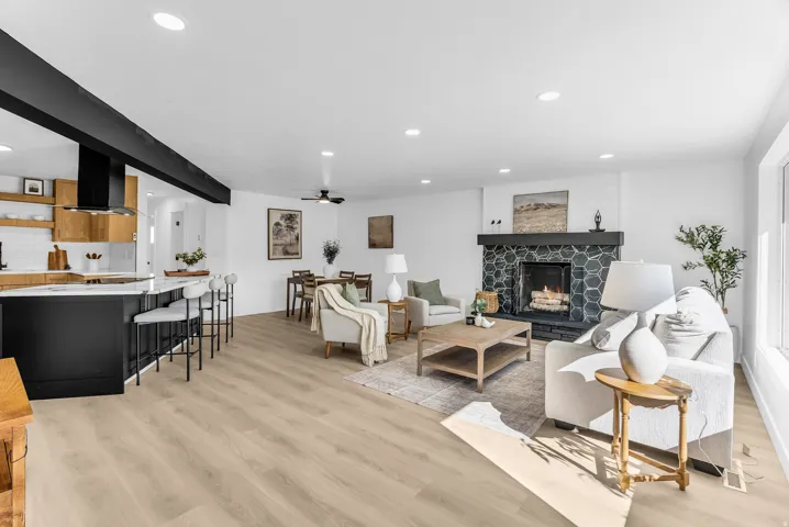 Spacious open-concept living area featuring light wood-finish flooring, recessed lighting, and a black hexagon-tiled fireplace