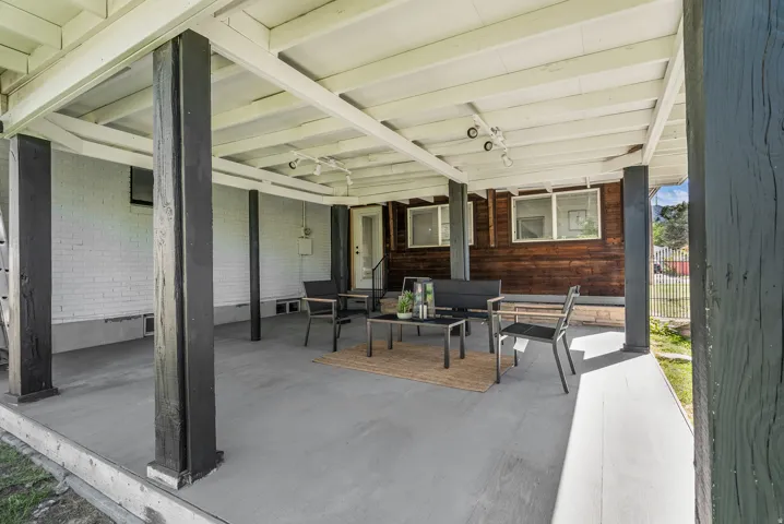 Covered patio featuring a painted concrete floor, exposed white ceiling joists, track lighting, and dark wood-paneled exterior