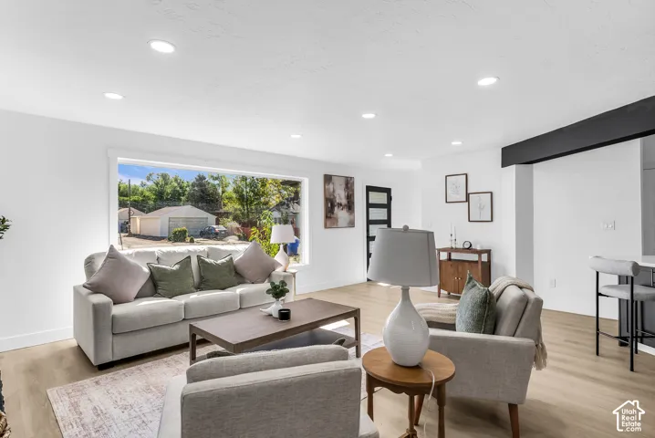 Recessed ceiling lighting, expansive window, wood-finish flooring, white walls, and a black accent beam