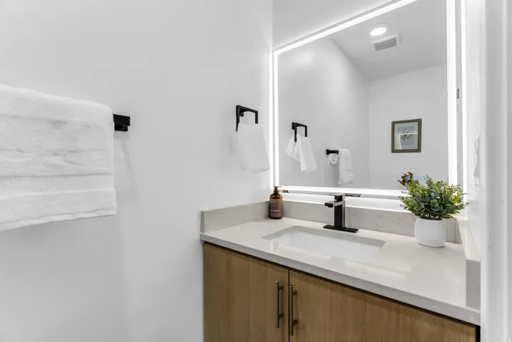 Master suite with lighted vanity mirror, integrated sink, stone-finish countertop, wood-finish cabinetry, and matte black fixtures