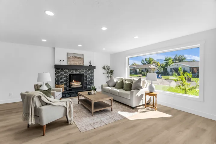 Living area featuring wood-finish flooring, a large picture window, recessed lighting, and a fireplace with a hexagonal tile surround and dark mantel