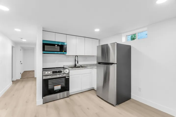 Full-size stainless steel refrigerator, white cabinetry, integrated stainless steel range with overhead microwave, and wood-finish flooring