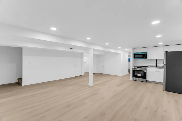 Second kitchen, open-concept living area with wood-finish flooring, recessed lighting, and a kitchen featuring white cabinetry, stainless steel appliances, and a black refrigerator