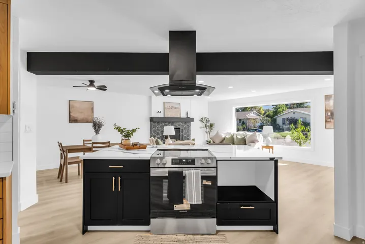 Kitchen island with a built-in stainless steel range, a black range hood, white countertops, and black cabinetry with gold-finish hardware