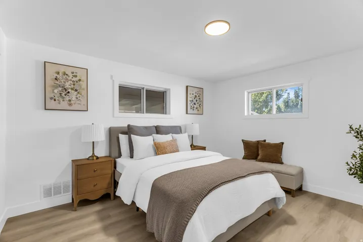 Bright room with white walls, wood-finish flooring, two windows, and a flush-mount ceiling light