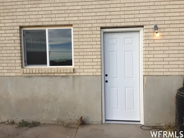 Beige brick exterior with a white paneled door, a single-paned window, and a wall-mounted light fixture