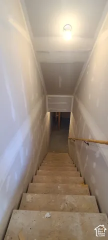 Staircase with wood handrail and overhead lighting, leading to an unfinished lower level