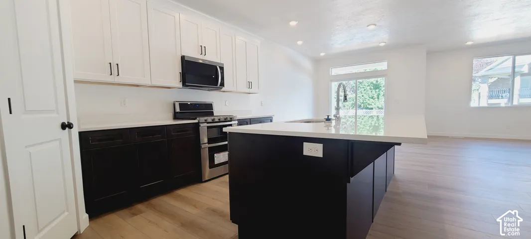 Kitchen featuring two-tone cabinetry, stainless steel appliances, a large island with an undermount sink, and wood-finish flooring
