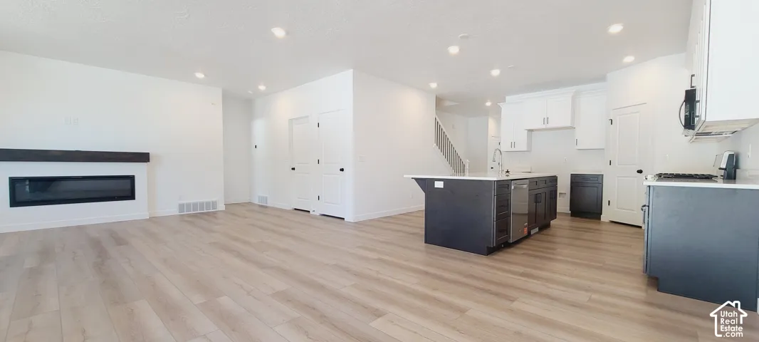 Open-concept living area with wood-finish flooring, recessed lighting, and a modern fireplace with a dark mantel