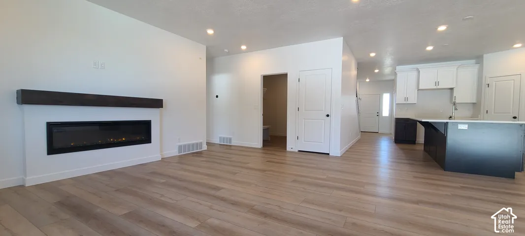 Recessed lighting, wood-finish flooring, linear electric fireplace with wood mantel, white shaker-style cabinetry, and a kitchen island with dark base cabinetry