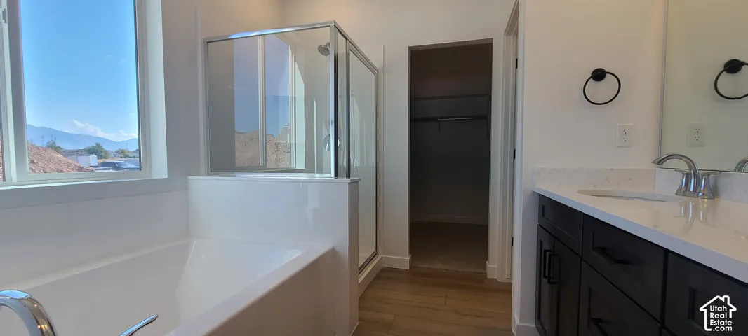 Soaking tub with chrome fixtures, glass-enclosed shower, wood-finish flooring, dark wood-finish vanity with dual sinks, and white countertop
