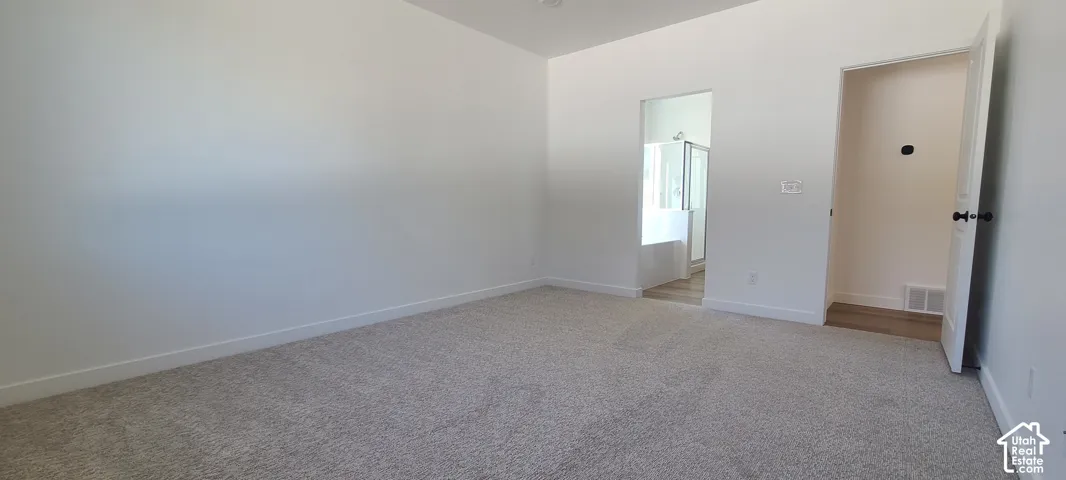 Spacious room with light neutral carpeting, a recessed ceiling light, and a doorway leading to a bathroom with a tub and shower