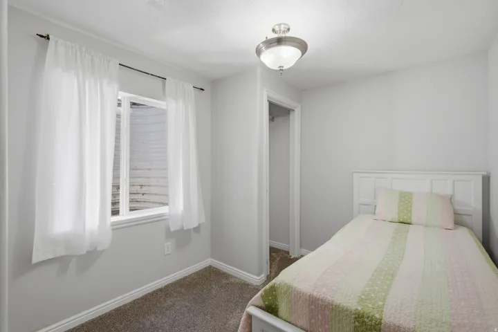 Basement bedroom 2. Neutral wall color, window with white trim, flush mount ceiling light fixture, carpeted flooring, and a closet with an open doorway