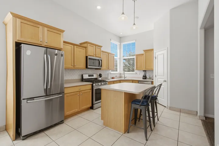Kitchen featuring light wood cabinetry, stainless steel appliances, a white tile backsplash, a central island, and high ceilings