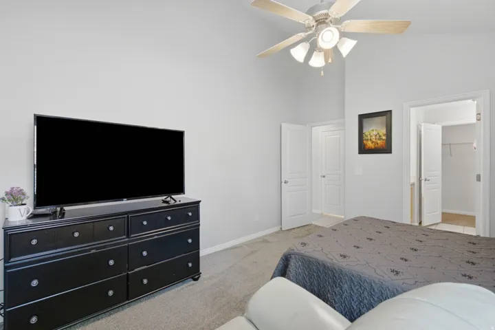Vaulted ceiling with a ceiling fan, light gray wall paint, and carpet flooring
