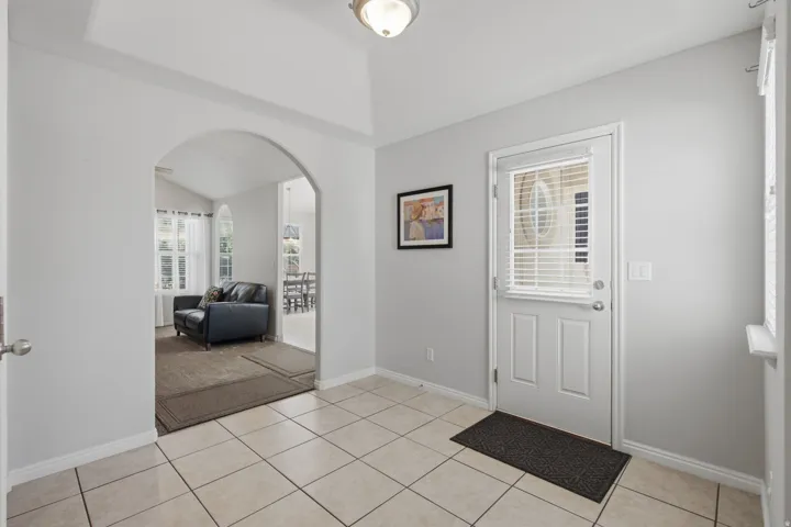 Tiled entry with arched doorway, overhead lighting, and a white paneled door with integrated blinds